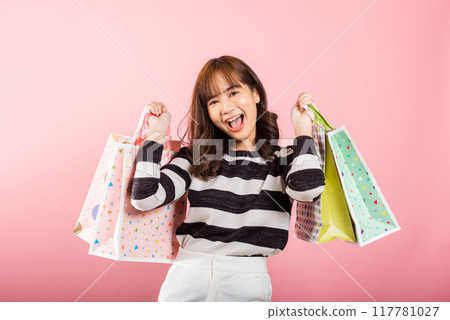 Portrait of Asian happy beautiful young woman teen shopper smiling standing excited holding online shopping bags colorful multicolor in summer, studio shot isolated on pink background with copy space 117781027