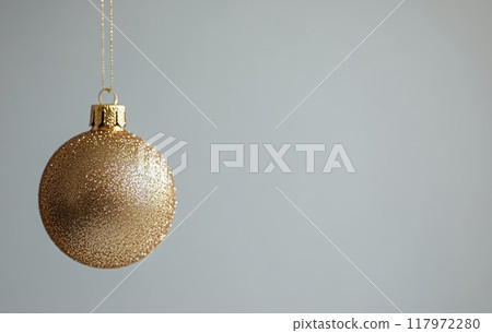 Elegant gold Christmas ornament hanging against a minimalist light gray background 117972280