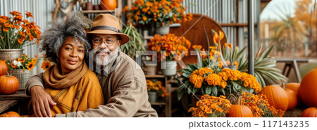 Senior black farmer couple with autumn pumpkin. African american older people near garden. Happy mature family with Thanksgiving or Halloween fall vegetables and flowers. Adults in gardening backyard 117143235