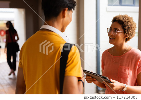 Talking in high school hallway, students holding tablet and backpack, smiling 117214303