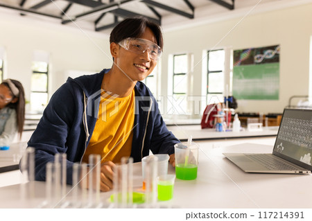 Conducting science experiment with laptop and test tubes, teenager in high school classroom 117214391