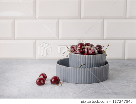 Juicy cherries berries  in a gray bowl on a white kitchen brick  background. Front view  117247843