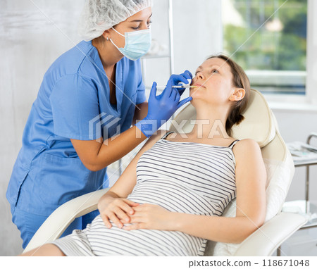 Young female cosmetologist makes injection in lips of patient 118671048