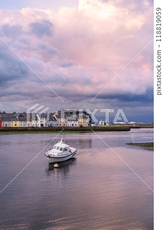 Vertical shot of Galway City at sunset with a boat in calm waters, under soft pink and grey clouds 118819059