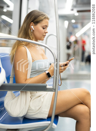 Young woman is sitting in subway car with headphones and phone, getting to work 118862088