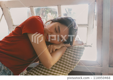 Sleepy woman in red t-shirt resting in the living room near the windows. 118950468