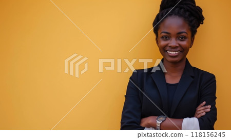 Woman in black suit standing in front of yellow wall, smiling with crossed arms 118156245