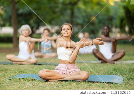 Girl stretching in lotus position during group yoga class in park 118162655