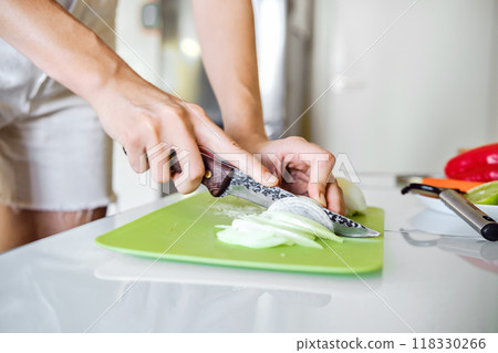 Unrecognizable person skillfully slices onion on a cutting board in a bright, modern kitchen 118330266