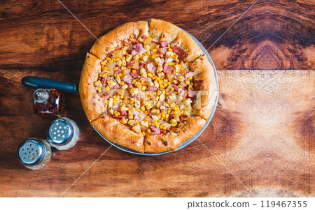 Top view of ham and corn pizza on wooden table. Ham pizza with corn on wooden background 119467355