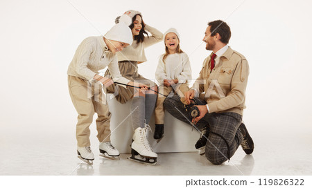 Father kneeling down to help his young daughter lace up her ice skates. Cozy caring moment showcases family love and winter traditions 119826322