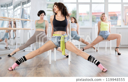 Group of women in high heels rehearsing dance while sitting on chair 119948555