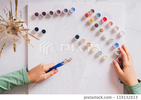 Girl's hands holding brushes and paints for painting by numbers top view 119132813