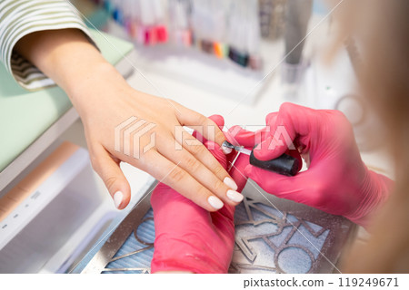 Nail stylist in pink gloves applying a top layer of gel polish to give the customers nails a flawless finish. 119249671