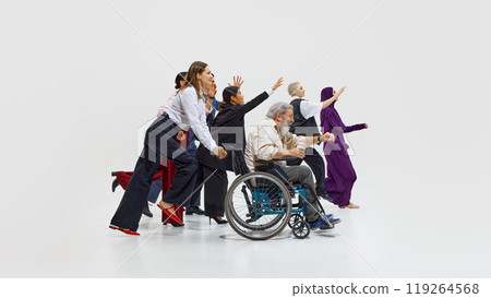 Diverse group of individuals, including one in wheelchair, all energetically reaching forward in motion against white studio background. 119264568