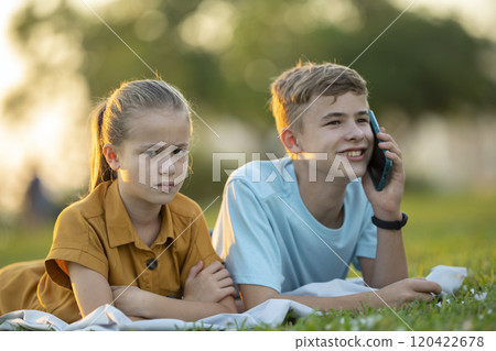 Happy young boy chatting on mobile phone ignoring his bored friend. Teenager friends having hard time communicating with each other. Friendship problems concept 120422678