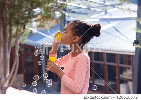 Blowing bubbles, african american girl enjoying outdoor activity at school playground with friends 120616579