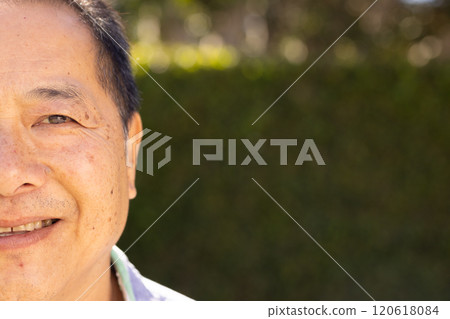 Smiling asian middle-aged man outdoors with greenery in background, enjoying sunny day 120618084