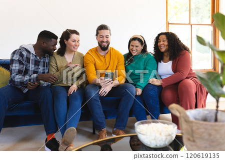 Happy diverse male and female friends relaxing at home together talking and looking at smartphone 120619135