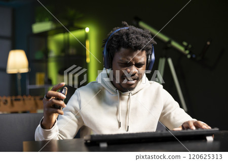 African american player shouting after failing to win videogame while playing on gaming PC. Upset gamer at computer desktop in apartment feeling like smashing desk, raging after game over 120625313