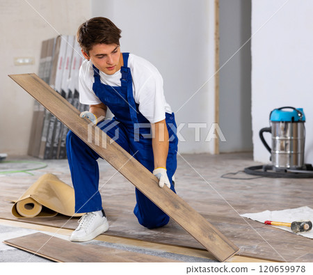 Professional young builder laying laminate flooring in repairable room 120659978