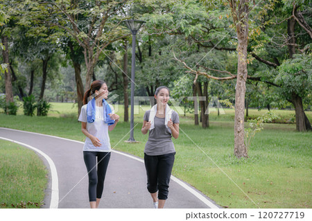 Two women jogging in a lush green park. 120727719