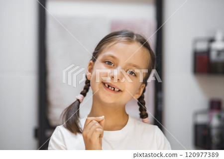 Portrait of cheerful Caucasian girl showing freshly fallen tooth. She smiles while looking in bathroom mirror. Youthful pride and childhood milestone captured. 120977389