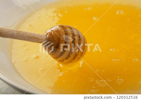 Close up wooden dipper in honey bowl 120312516