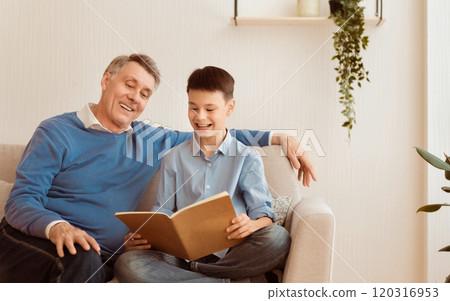 Cheerful Grandfather Reading Book With Grandson Boy Doing Homework Together Sitting On Sofa At Home. Selective Focus, Free Space 120316953