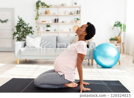 Side view of black pregnant woman doing backbend during meditation or yoga at home. Beautiful African American expectant lady stretching at time of her breathing practice indoors 120324815