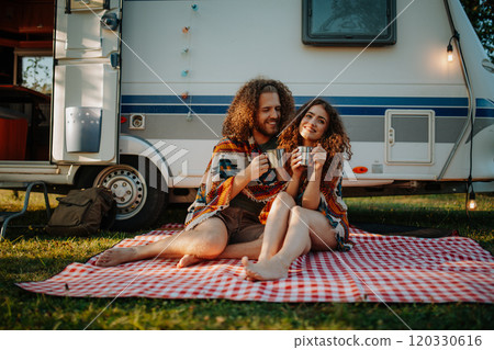 Beautiful couple sitting in front of caravan under blanket, enjoying peaceful moment, drinking coffee of herbal tea. 120330616