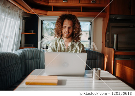 Young man working remotely from caravan. Man using camper as homeoffice, working on notebook. 120330618