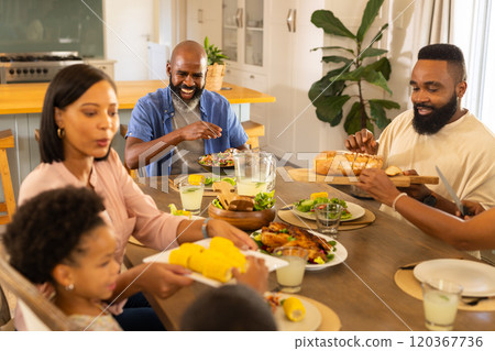 multigenerational family enjoying dinner together, sharing food and smiling around dining table 120367736