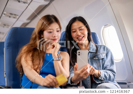 Two female friends are on the flight, one holding a credit card and the other holding a phone. 121416367