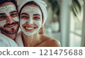 A young couple wearing white towels smiles. Their faces with skincare products.  121475688