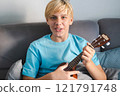 Laughing teenager playing ukulele, at home. 121791748