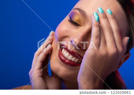 Caucasian woman with brown hair wearing golden eye shadow and blue nail polish on blue background 121020061