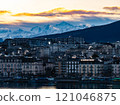 Geneva's cityscape at sunrise features smoking chimneys, waterfront buildings, and Mont Blanc mountain range in the Alps, creating a breathtaking winter scene 121046875