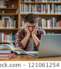 Young caucasian male student feeling stressed in library surrounded by books and laptop 121061254