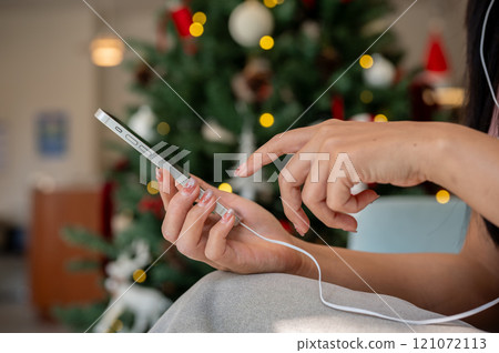 A woman sits in a coffee shop, using her smartphone and listening to music on her earphones. 121072113