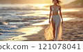 A beautiful female tourist in a light white dress walks along the beach. 121078041