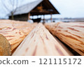 Close-up view of wooden logs with a workshop in the background, highlighting the textures and natural patterns of the wood 121115172