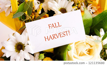 The concept of holidays. The phrase FALL HARVEST on a white card in a bouquet of flowers, close-up, front view 121135680