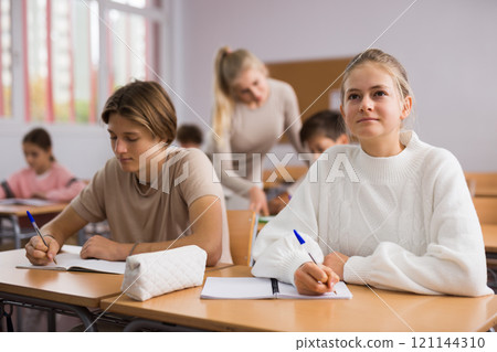 Teenage pupils sitting at desk in classroom 121144310