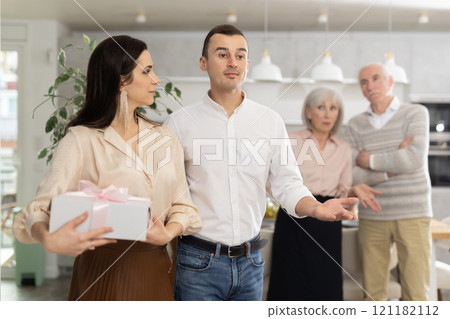 Man welcoming woman home with displeased elderly parents observing 121182112