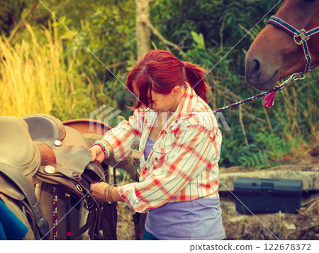 Cowgirl getting horse ready for ride on countryside 122678372