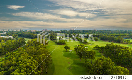 A panoramic view of a golf course with lush greenery and a cloudy sky 122109373