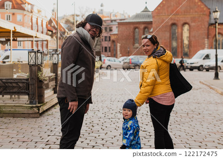 Parents walking hand in hand with their son through the charming city streets, enjoying the warmth of the season and creating joyful memories together 122172475