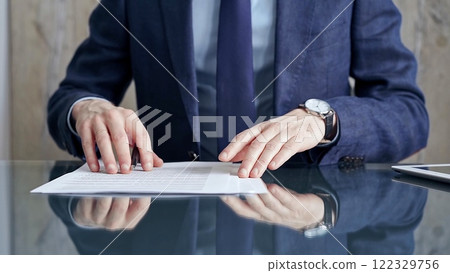 Businessman reviewing documents at office desk. Close-up of a professional man's hands examining paperwork with pen and tablet in sight. Business people concept 122329756