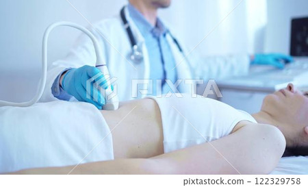 Doctor man wearing a blue medical gloves using an ultrasound equipment on a female patient lying down in clinic cabinet. Medicine concept 122329758